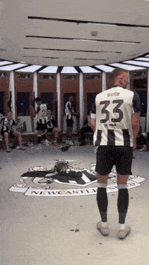 a man in a number 33 jersey stands in a newcastle locker room