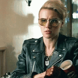 a woman wearing sunglasses and a black leather jacket is holding a cup of coffee .