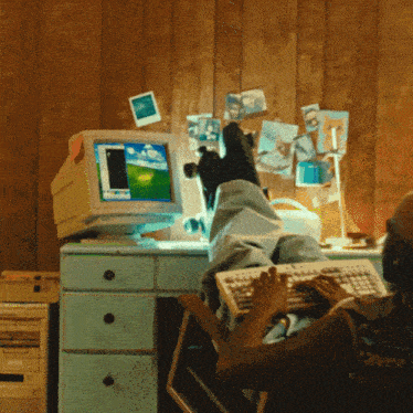 a person sitting at a desk with their feet up using a keyboard and a computer with a windows screen