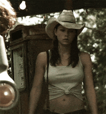a woman wearing a cowboy hat stands in front of a telephone