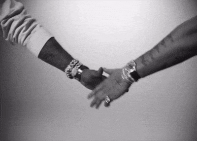 a black and white photo of two people holding hands .