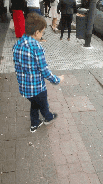 a young boy wearing a blue plaid shirt is walking down a sidewalk