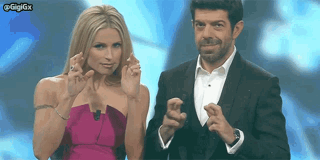 a woman in a pink dress and a man in a tuxedo are making a heart shape with their hands ..
