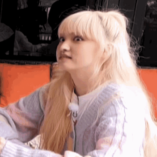 a woman with blonde hair is sitting on a couch wearing a sweater and making a face .