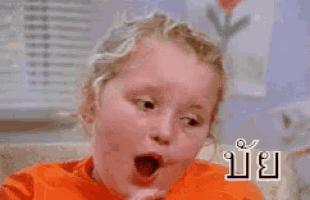a little girl in an orange shirt is making a funny face and smiling .