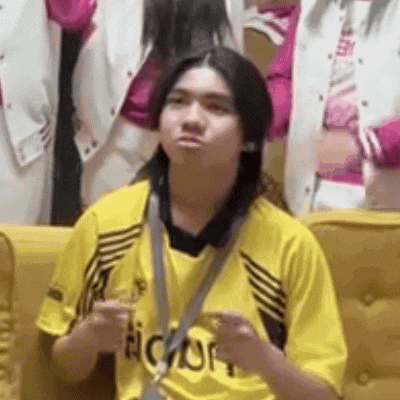 a young man in a yellow shirt is sitting on a yellow couch with his hands in the air .