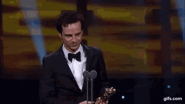 a man in a tuxedo is holding a trophy in front of a microphone .