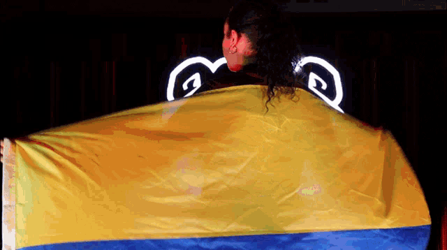 a woman holds a yellow and blue flag in front of a sign that says ' g ' on it