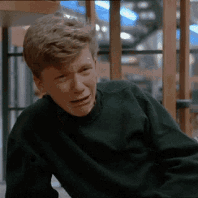 a young man in a green sweater is making a sad face