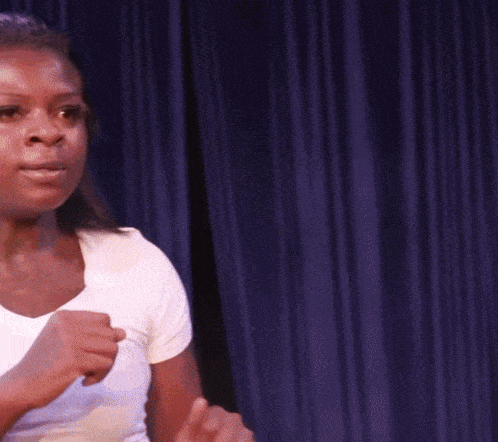 a woman in a white shirt is standing in front of a blue curtain with her fist in the air