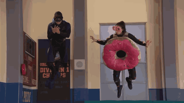 a woman in a donut costume is jumping in the air while a man watches