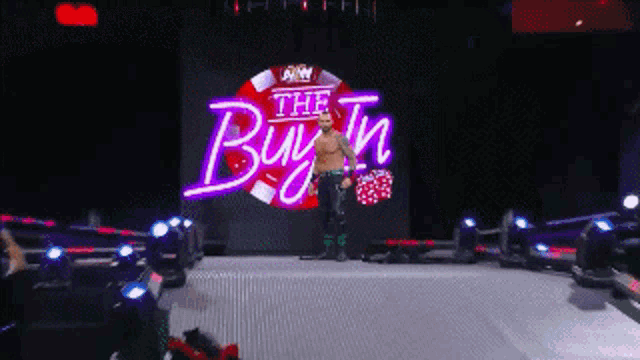 a wrestler stands in front of a large screen that says the buy in