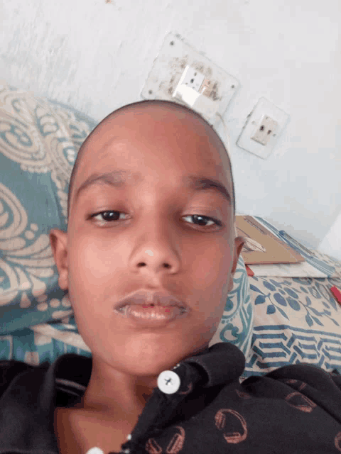 a young boy with a shaved head is laying on a bed and looking at the camera