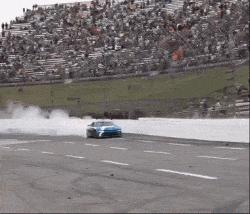 a race car is drifting on a race track with a crowd watching .