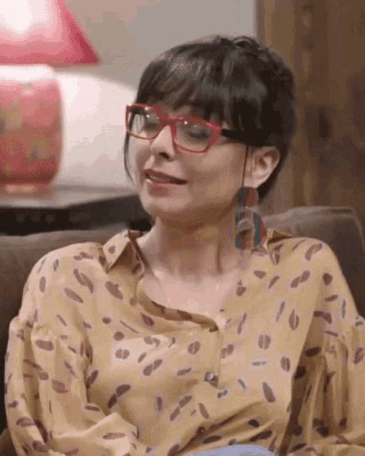 a woman wearing glasses is sitting on a couch and smiling .
