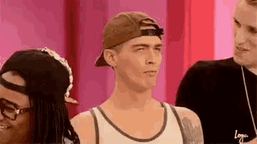 a man wearing a baseball cap and a tank top is standing in front of a pink wall .