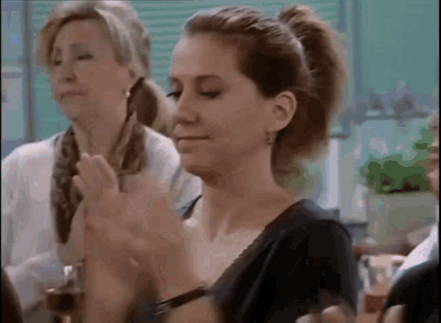 a woman in a ponytail is clapping her hands in a room with other women .