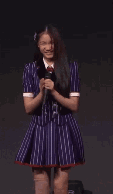 a girl in a purple striped dress is holding a microphone and smiling .