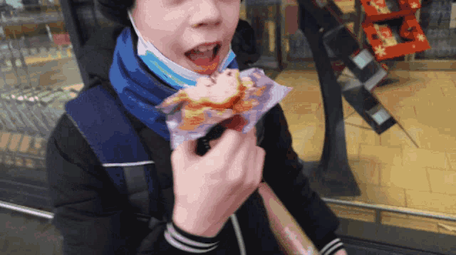 a young boy wearing a mask is eating a sandwich