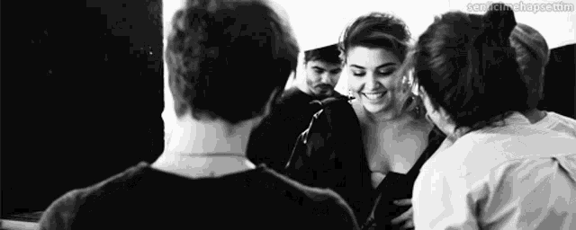 a black and white photo of a group of people standing around a woman in a black dress .