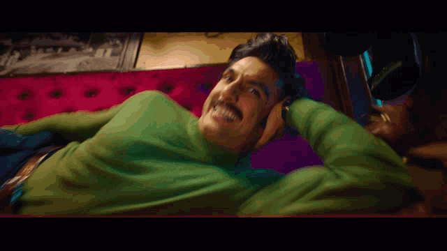 a man wearing a green turtleneck is laying on a couch