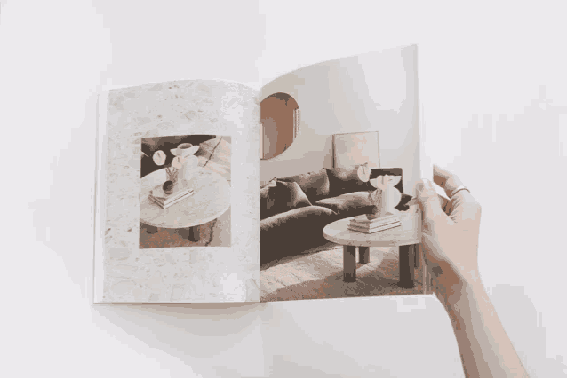 a person is holding a book with a picture of a couch and a table