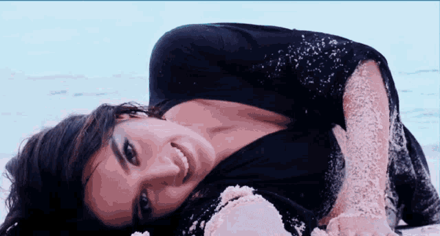 a woman in a black shirt is laying on the beach