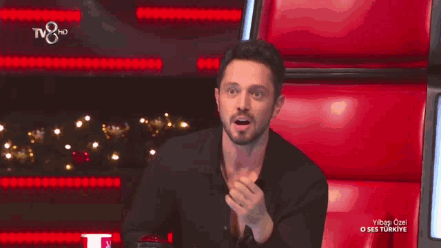 a man in a black shirt is sitting in a red chair with a tv8 hd logo above him