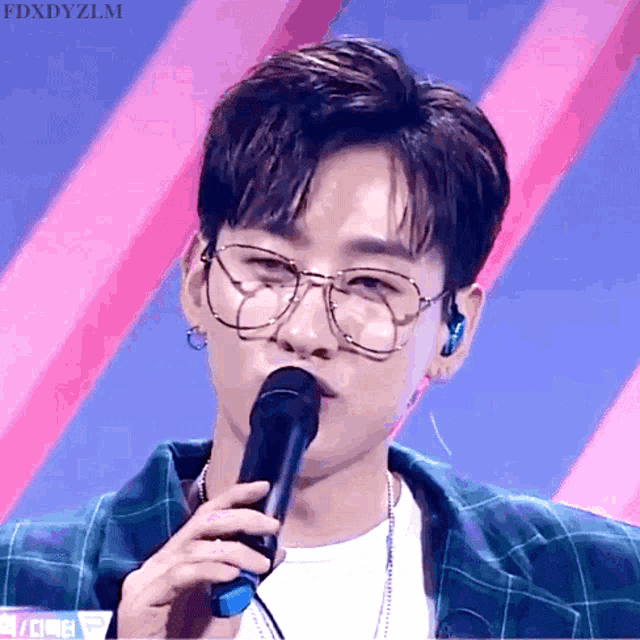 a young man wearing glasses is singing into a microphone with the name fdxdyzlm on the bottom right