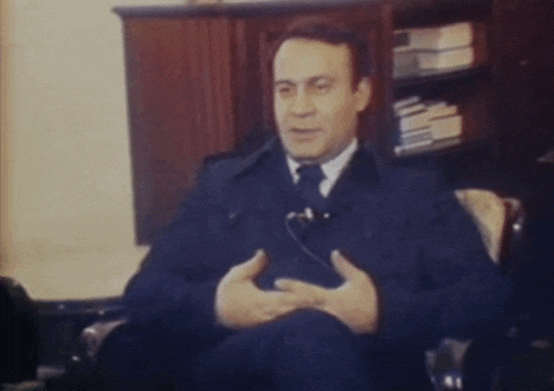 a man in a suit and tie is sitting in a chair talking to someone