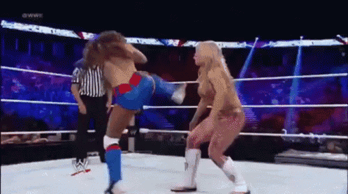 two women are wrestling in a ring with a referee in the background .