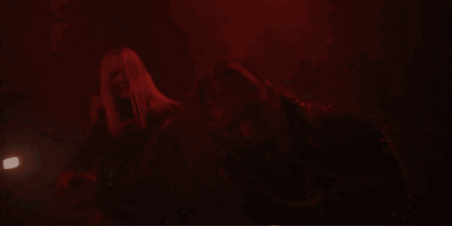 a woman is squatting in front of a man in a dark room .