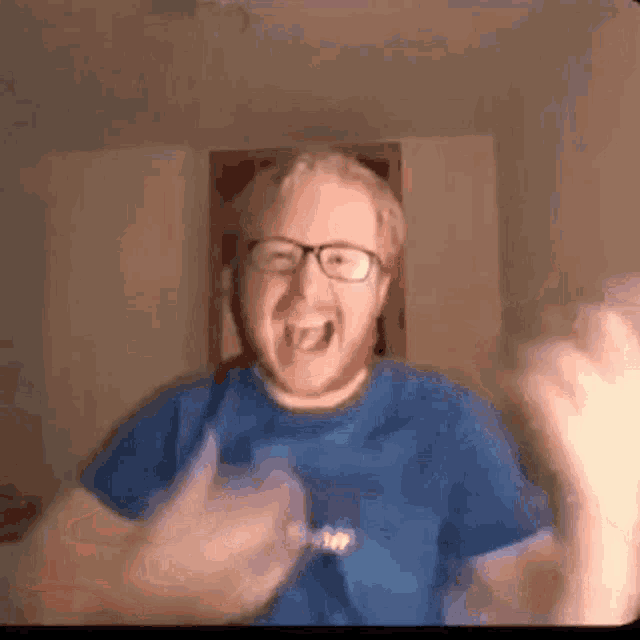 the man is wearing glasses and a blue shirt and is giving a thumbs up .