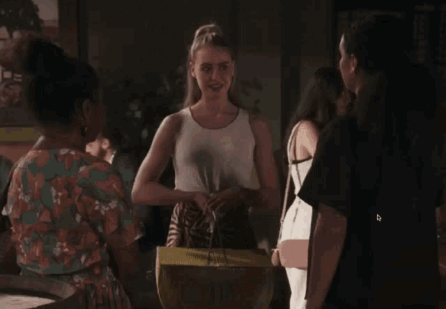 a woman in a white tank top is standing in a room with other women