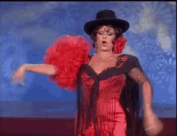 a woman in a red dress and a black hat is dancing on a stage .