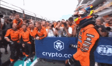 a race car driver is walking in front of a crowd of people with a sign that says crypto.co.
