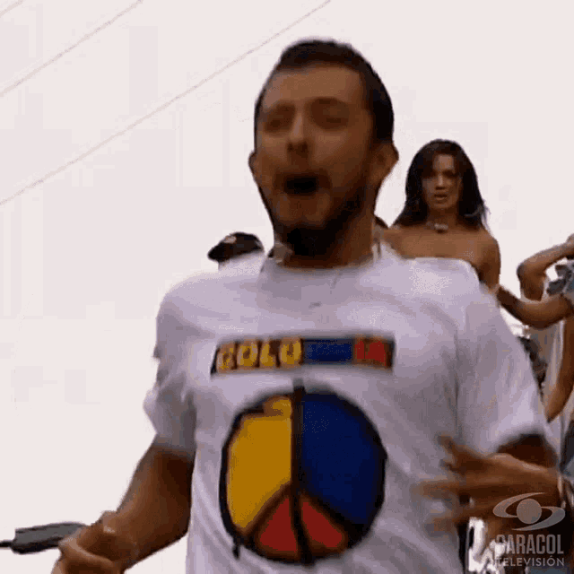 a man wearing a white t-shirt with a peace sign on it is dancing in front of a group of people .