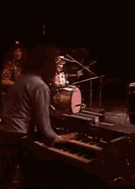 a man playing a keyboard in a dark room with a drum in the background