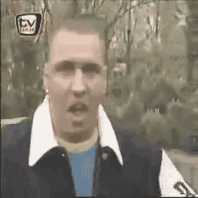 a man in a varsity jacket is making a funny face in front of trees .