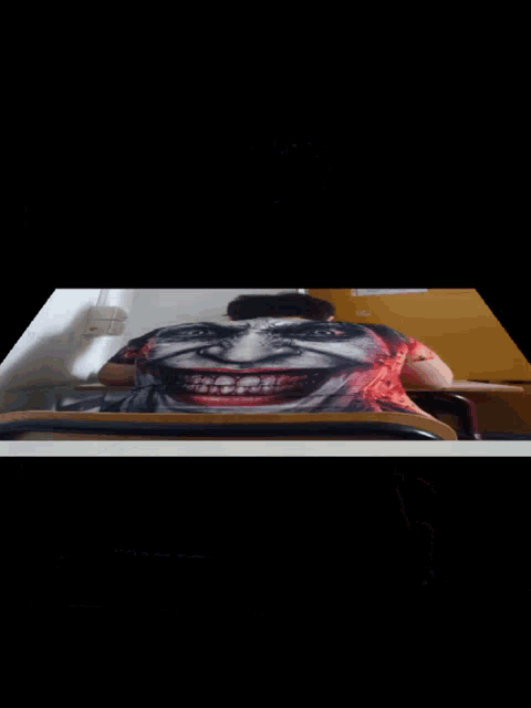 a man wearing a shirt with a joker face on it sits at a desk