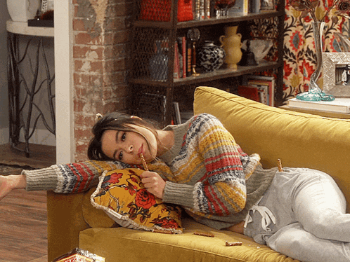 a woman laying on a yellow couch eating a sandwich