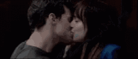a man and a woman are kissing in front of a dark background .