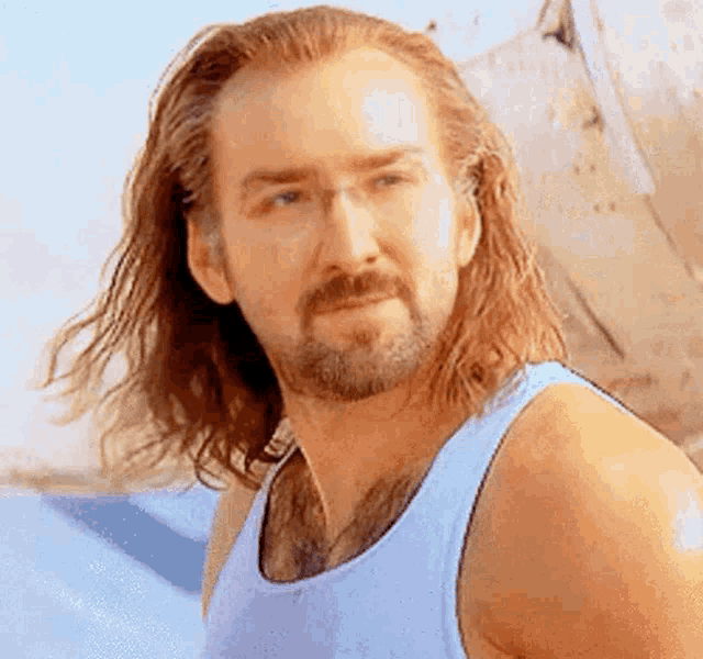 a man with long hair and a beard is wearing a tank top and looking at the camera .