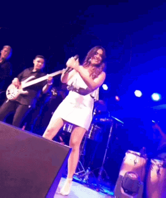 a woman in a white dress is singing into a microphone