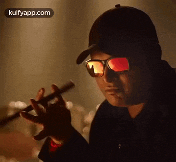 a man wearing sunglasses and a hat is holding a flute in his hand .
