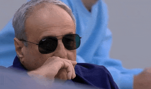 a man wearing ray-ban sunglasses is sitting with his hand on his chin .