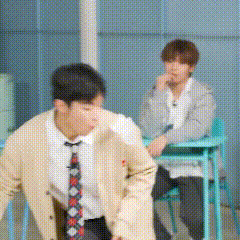 a man in a suit and tie is sitting at a desk with another man in a classroom .