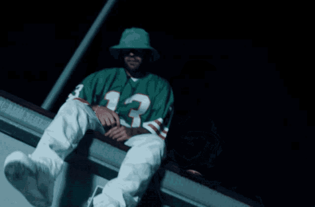 a man wearing a green jersey with the number 13 on it sits on a railing