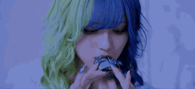 a girl with blue and green hair is holding a blue object in her hand