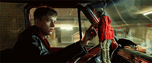 a man driving a car with a doll hanging from the steering wheel